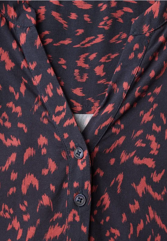 Blouse noire à motifs rouges abstraits, encolure en V et boutons.