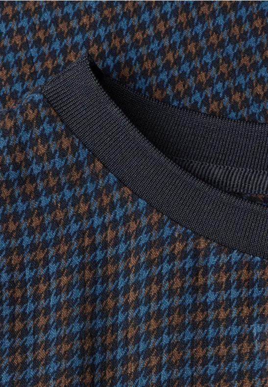 Nahaufnahme eines Strickpullovers mit blau-braunem Hahnentrittmuster und schwarzem Rippenstrickkragen.