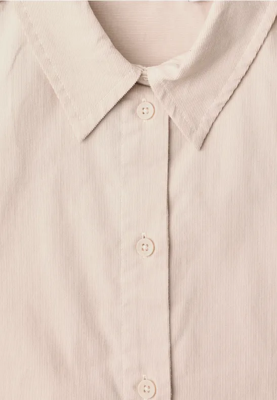 Gros plan d’une chemise beige clair avec col et patte de boutonnage.