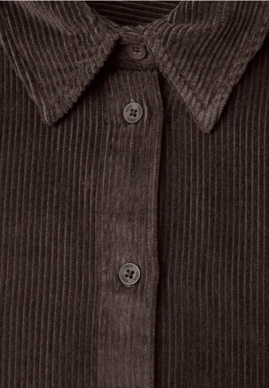 Nahaufnahme einer braunen Cordjacke mit sichtbarer Knopfleiste und Hemdkragen.