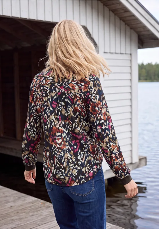 Une femme aux cheveux blonds, chemise colorée et jean, marche sur un ponton au bord du lac.