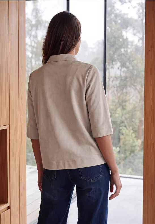 Frau steht mit dem Rücken zur Kamera, trägt helle 3/4-Arm-Bluse und blaue Jeans in modernem Raum.