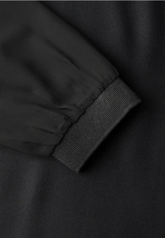 Nahaufnahme einer schwarzen Jacken-/Pullover-Ärmel mit elastischem Bündchen auf schwarzem Stoff.