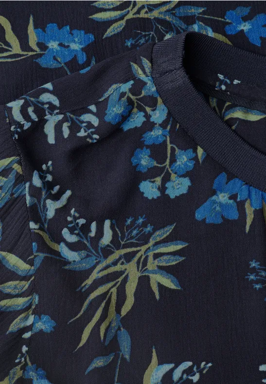 Nahaufnahme eines dunkelblauen Shirts mit blauen Blumen und grünen Blättern.