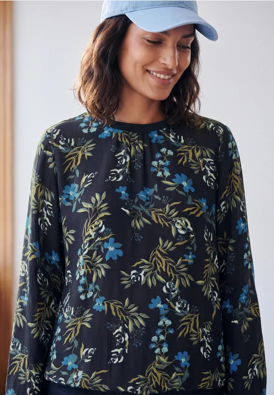 Eine Frau trägt eine blaue Kappe und ein schwarz-blau-grünes Blumenshirt