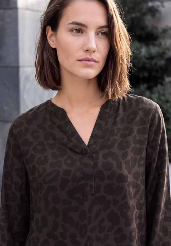 Jeune femme aux cheveux châtains courts, portant un chemisier sombre à motif léopard en ville.