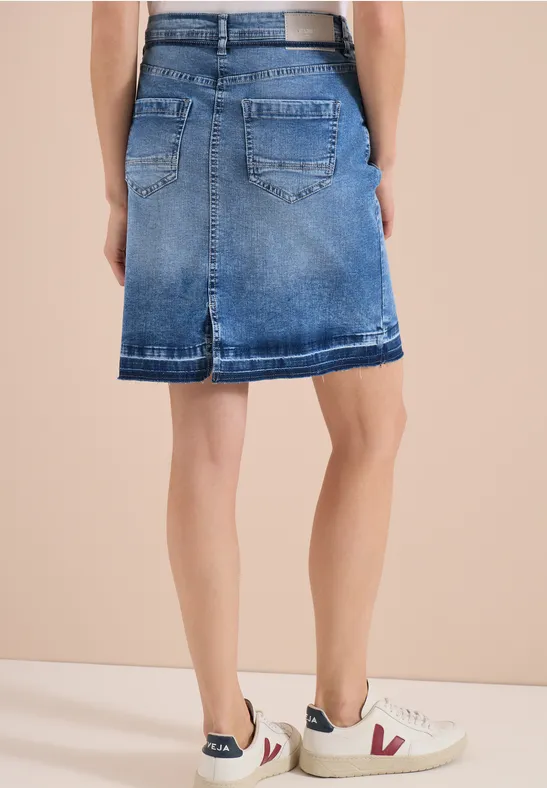 Rückansicht eines Models in mittellangem, blauem Jeansrock und weißen Sneakern.