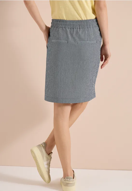 Frau trägt knielangen, gestreiften Rock mit elastischem Bund und Taschen, dazu gelbe Sneaker.