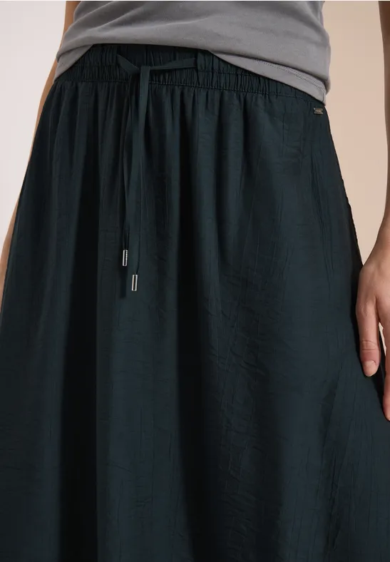 Persoon draagt een losse zwarte rok met trekkoord in de taille en een grijs t-shirt voor een lichte achtergrond.