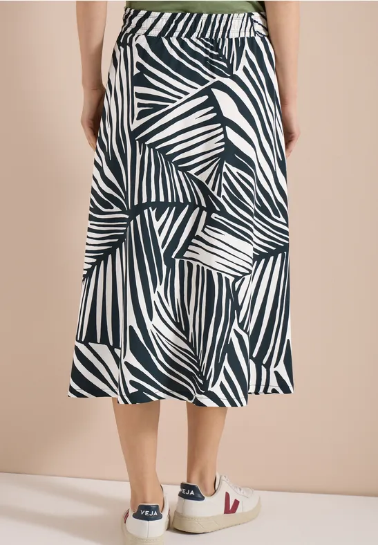 Witte midi-rok met zwart abstract bladprint, elastische tailleband, uitlopend model, gecombineerd met sneakers.