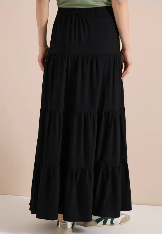 Rückenansicht eines langen schwarzen Stufenrocks mit Gummibund und Rüschen.