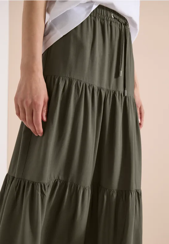 Nahaufnahme: Olivgrüner, stufiger Maxirock mit elastischem Bund und Volants.