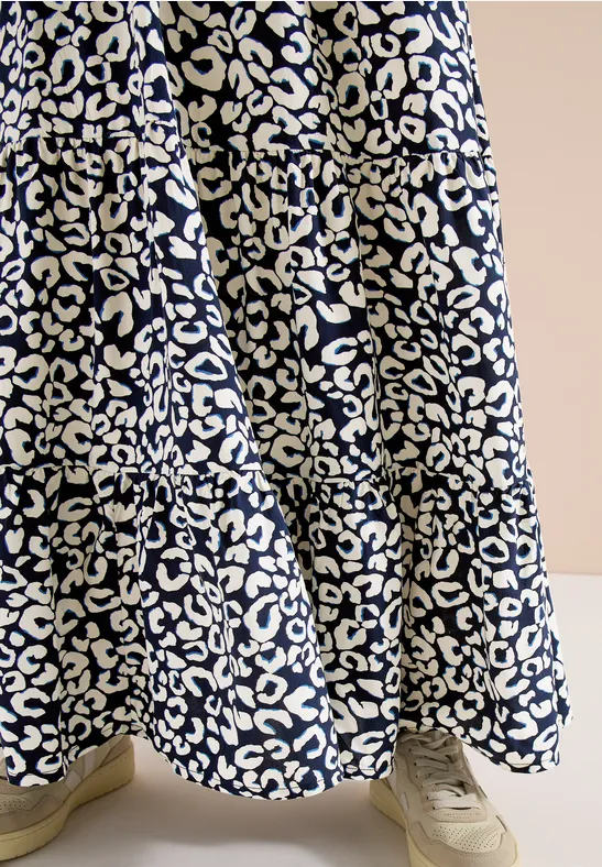 Weit schwingender Rock mit weißem Leopardenmuster auf dunkelblauem Stoff und hellen Sneakern.