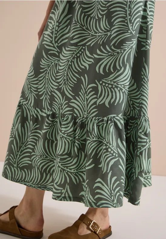Langes, grün gemustertes Stufenkleid im Blättermuster und braune Sandalen mit Schnalle.