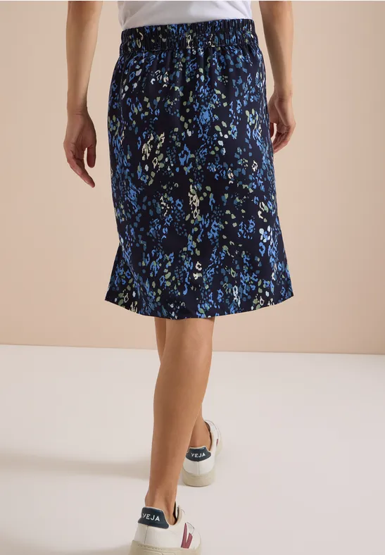 Achteraanzicht van een vrouw met een donkerblauwe, knielange bloemenrok en casual sneakers.