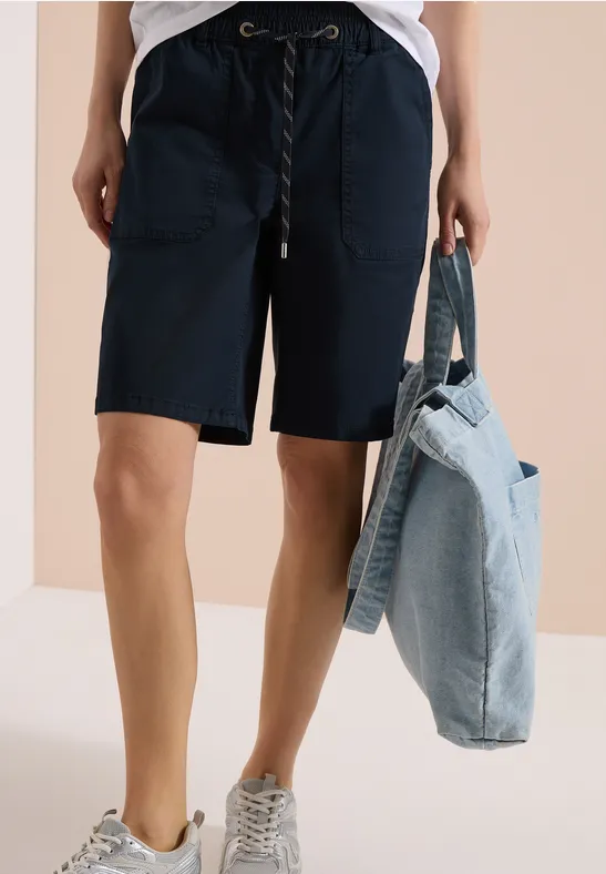 Persoon in donkerblauwe short, wit t-shirt en sneakers, met een lichtblauwe jeans tas.