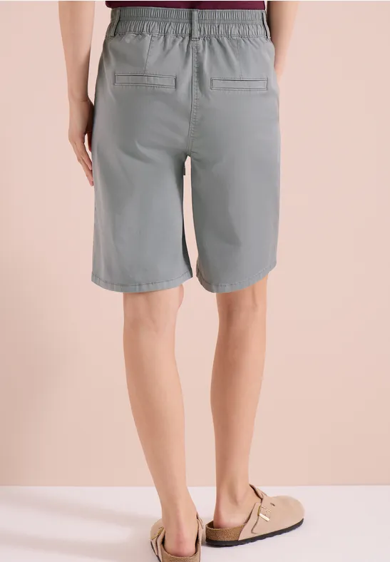 Achteraanzicht van een persoon in grijze bermudashorts en sandalen voor een beige achtergrond.