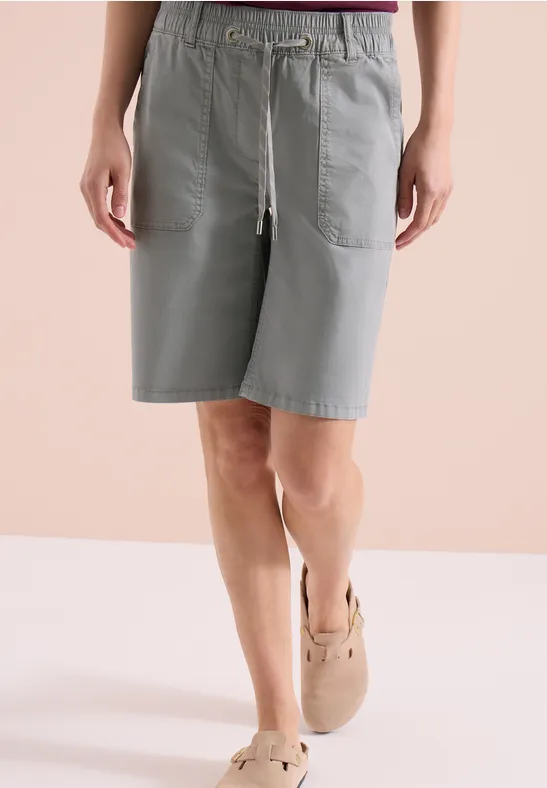 Persoon in lichtgrijze katoenen korte broek tot op de knie met tunnelkoord en zakken, met beige espadrilles.