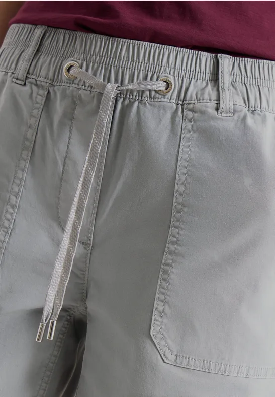 Close-up van een lichtgrijze broek met elastische taille, opgestikte zakken en contrastkleurige trekkoorden.