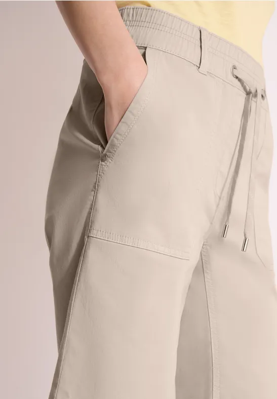 Close-up van een beige broek met trekkoord en hand in de zak.