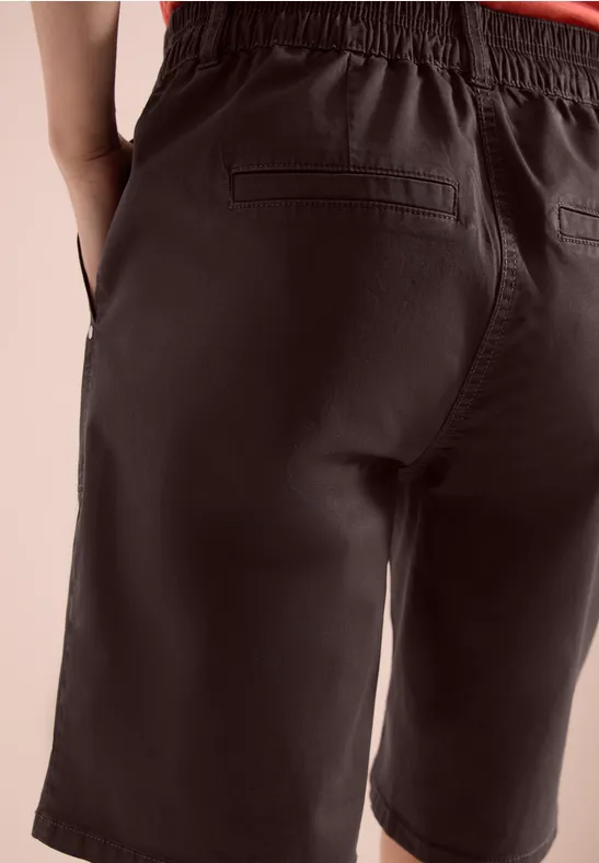 Achteraanzicht van een persoon in donkere, knielange short met achterzakken.