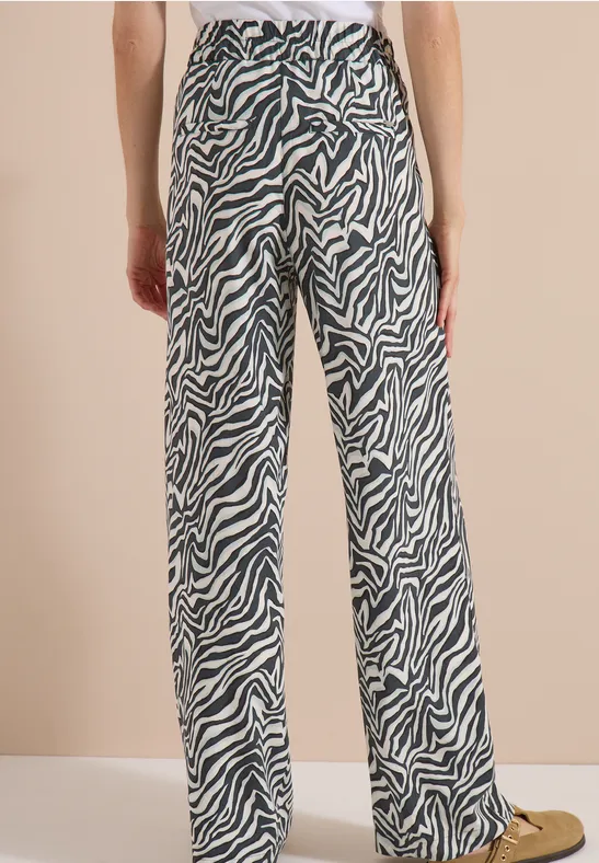 Femme de dos portant un pantalon large à imprimé zèbre noir et blanc sur fond beige.