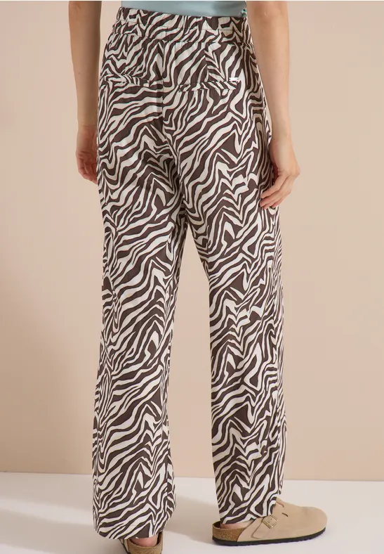 Beine einer Person in weiten, locker sitzenden Hose mit Zebra-Muster und beigen Schuhen.