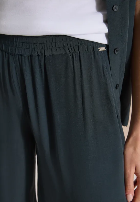 Detail: loszittende donkergroene broek met elastische taille, wit topje en donkergroene jas.