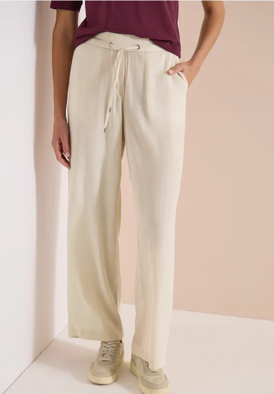 Personne porte un pantalon large beige à cordon et poches, associé à un haut bordeaux et des baskets.