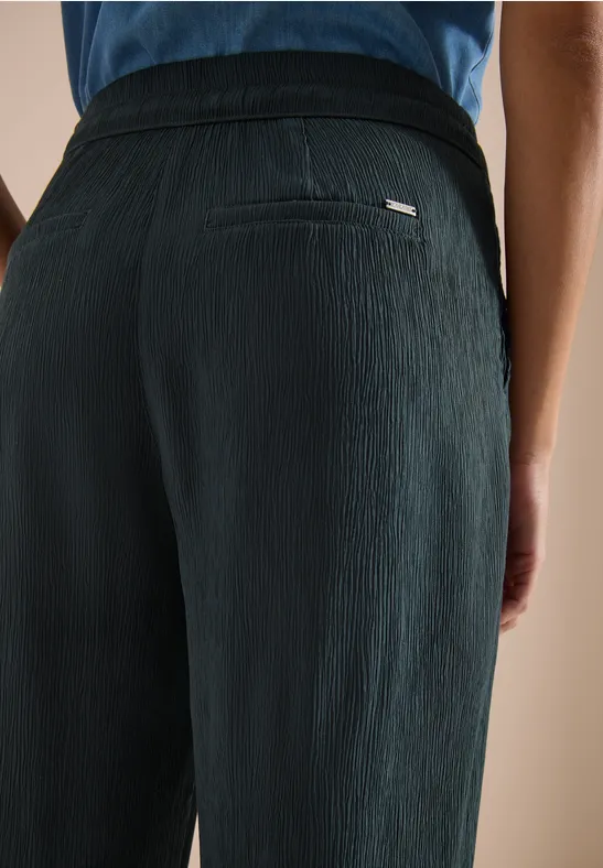 Person trägt schwarze, strukturierte Hose, Rückenansicht.