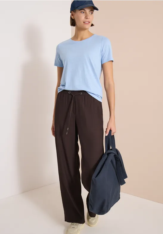 Eine Person in hellblauem T-Shirt und brauner Hose, hält eine dunkelblaue Tasche.