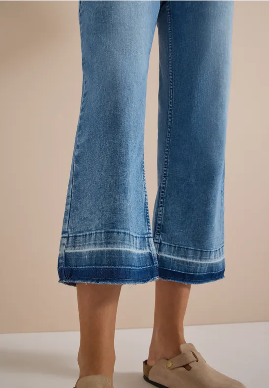 Wijde blauwe jeans-culotte met sierstiksels, gecombineerd met beige mules met gesp.