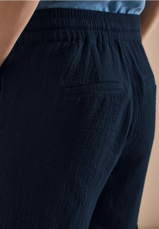 Nahaufnahme einer Person von hinten in dunkelblauer, texturierter Hose mit Tasche.