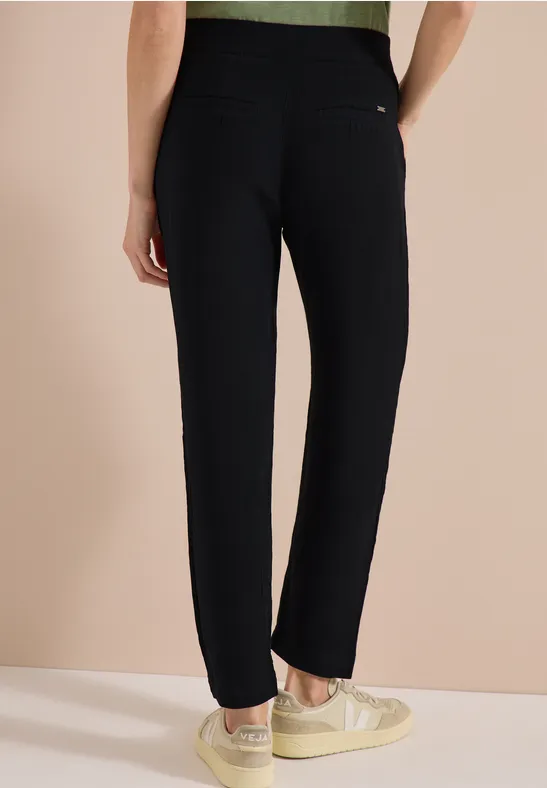 Iemand draagt een zwarte broek en lichte sneakers voor een neutrale, lichte achtergrond.