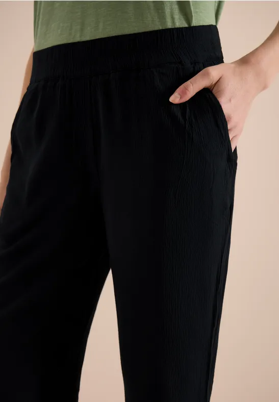 Zwarte, losse broek met elastische taille en zijzak, hand in zak