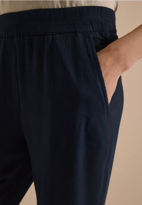 Donkerblauwe, losse broek met elastische taille en zijzak, hand in de zak.