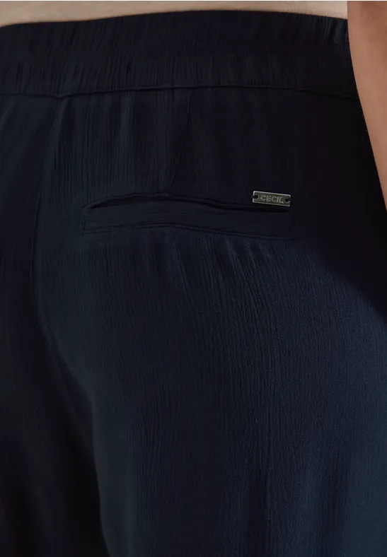 Achteraanzicht van donkerblauwe, gestructureerde broek met elastische tailleband en ritssluitingzak aan de achterkant.