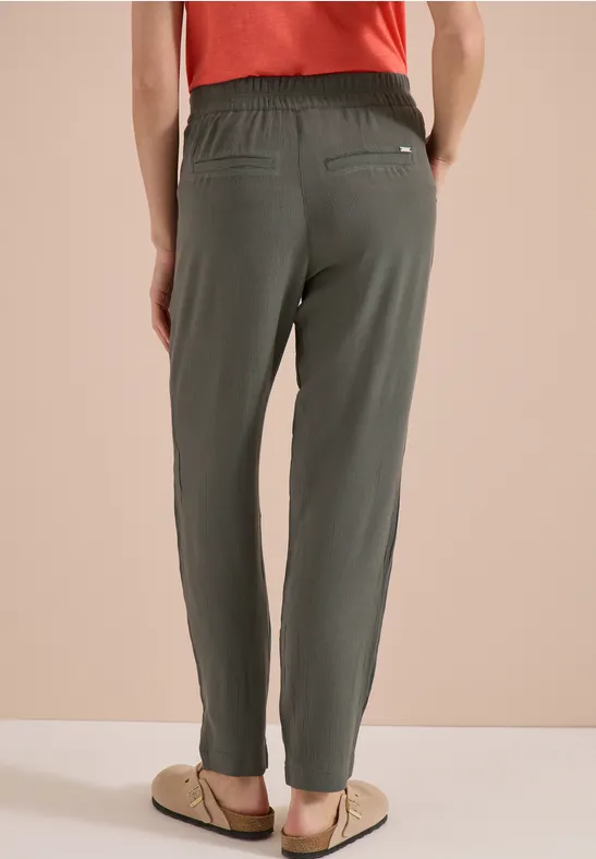 Achteraanzicht van een persoon met losse olijfgroene broek met elastische taille en sandalen.