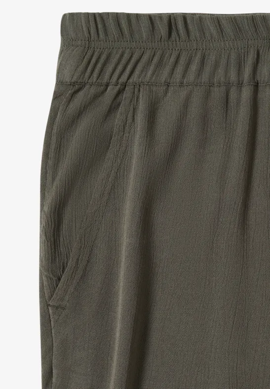 Close-up van een olijfgroene stofbroek met elastische tailleband en zijzak.