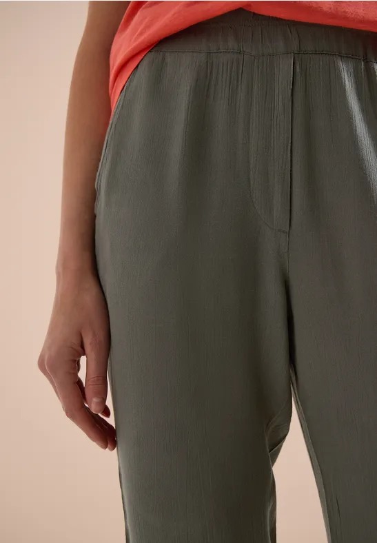 Close-up van een persoon in een loszittende groene broek en een rood topje.