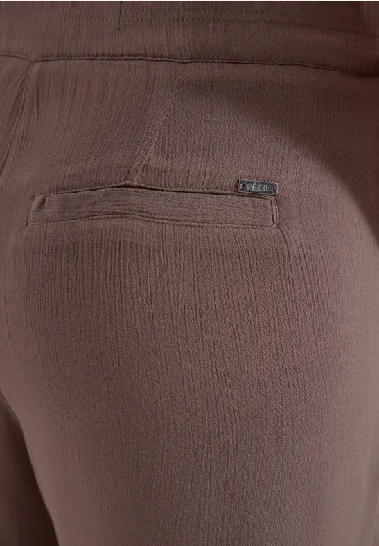 Close-up van een bruine broek met gestructureerde stof en een ritssluiting op de achterkant.