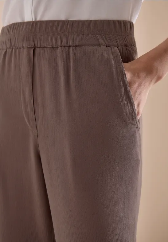 Bruine vrijetijdsbroek met elastische tailleband en zijzakken, hand in de zak gestoken.