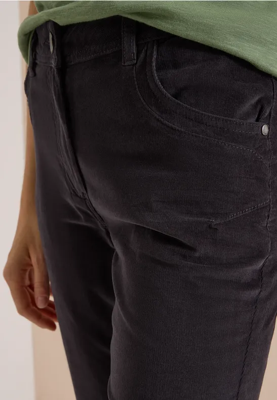 Gros plan sur une personne en jean noir et haut vert, main posée sur la hanche.