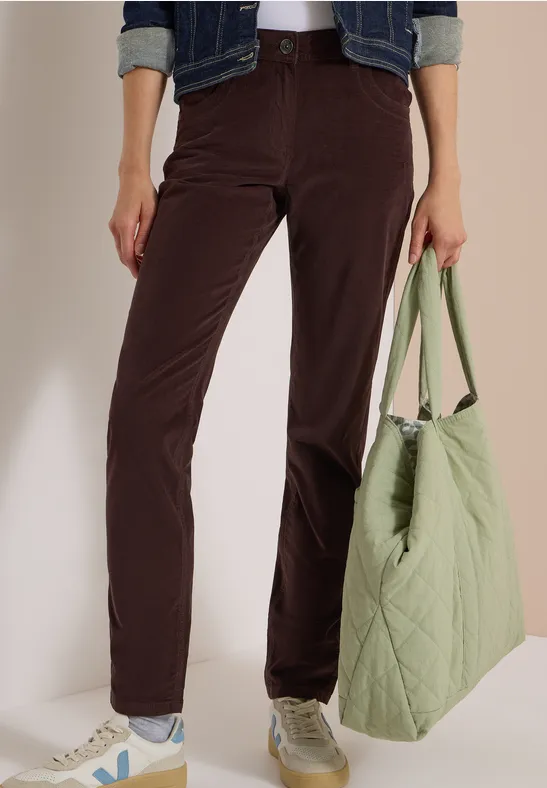 Person trägt dunkelbraune Cordhose, weiße Sneaker und hält eine hellgrüne gesteppte Tasche.
