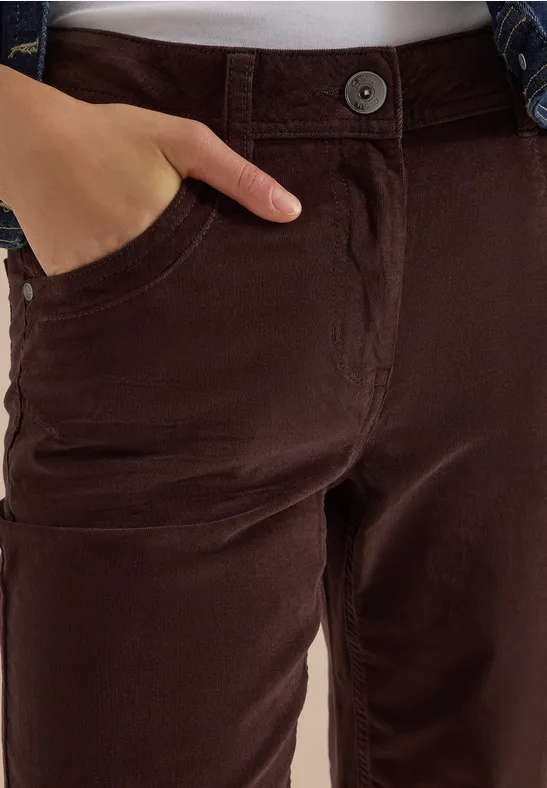 Nahaufnahme: dunkelbraune Hose mit Tasche, Hand steckt hinein, darüber teilweise Jeansjacke.