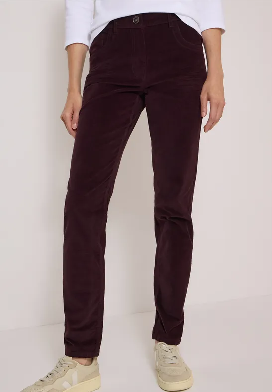Personne portant un pantalon en velours côtelé bordeaux, haut blanc et baskets claires.