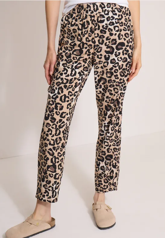 Beine in schmal geschnittenen, beige Leopardenmuster-Hosen und beigen Slippers.