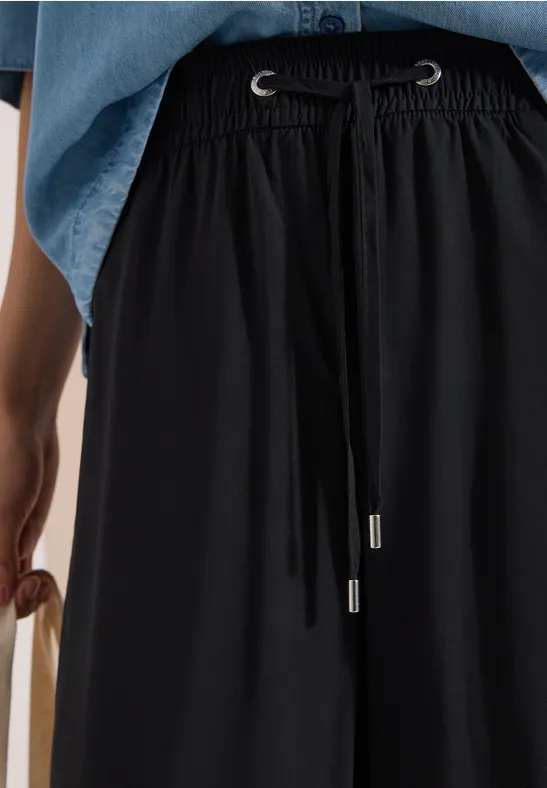 Schwarze, weite Stoffhose mit Tunnelzugbund, kombiniert mit Jeanshemd und seitlich gehaltener Tasche.