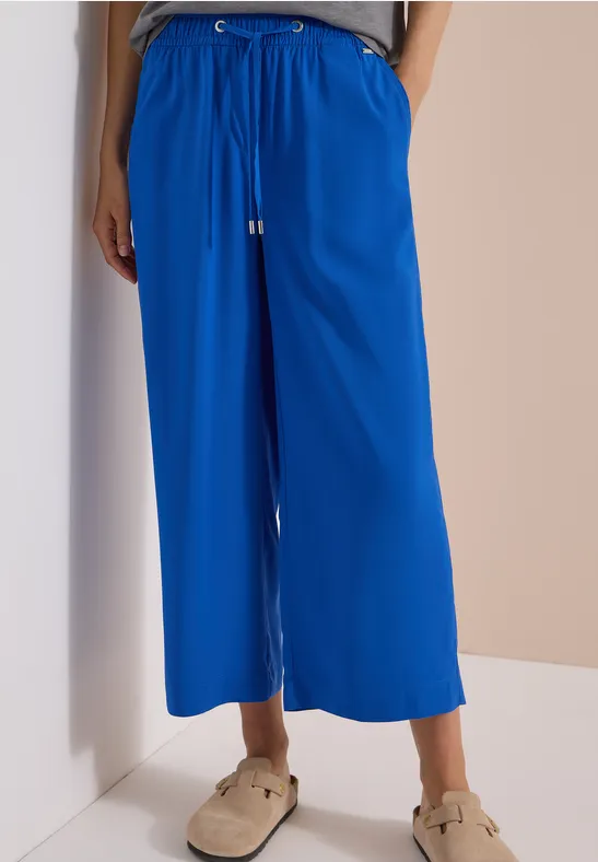Knöchellange, weite blaue Hose mit Kordelzug und Taschen, dazu Sandalen