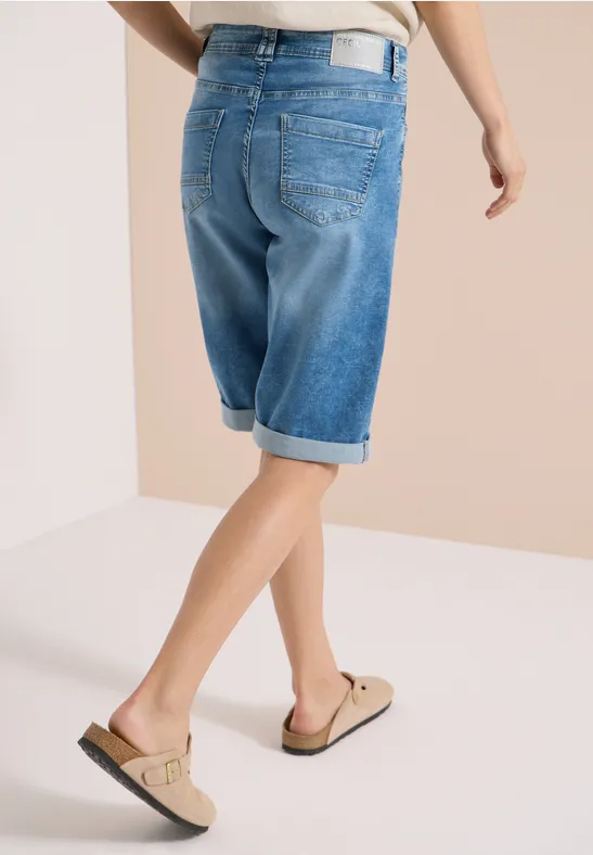 Person mit hellblauen Jeans-Shorts knielang und beigen Sandalen, seitliche Rückenansicht.